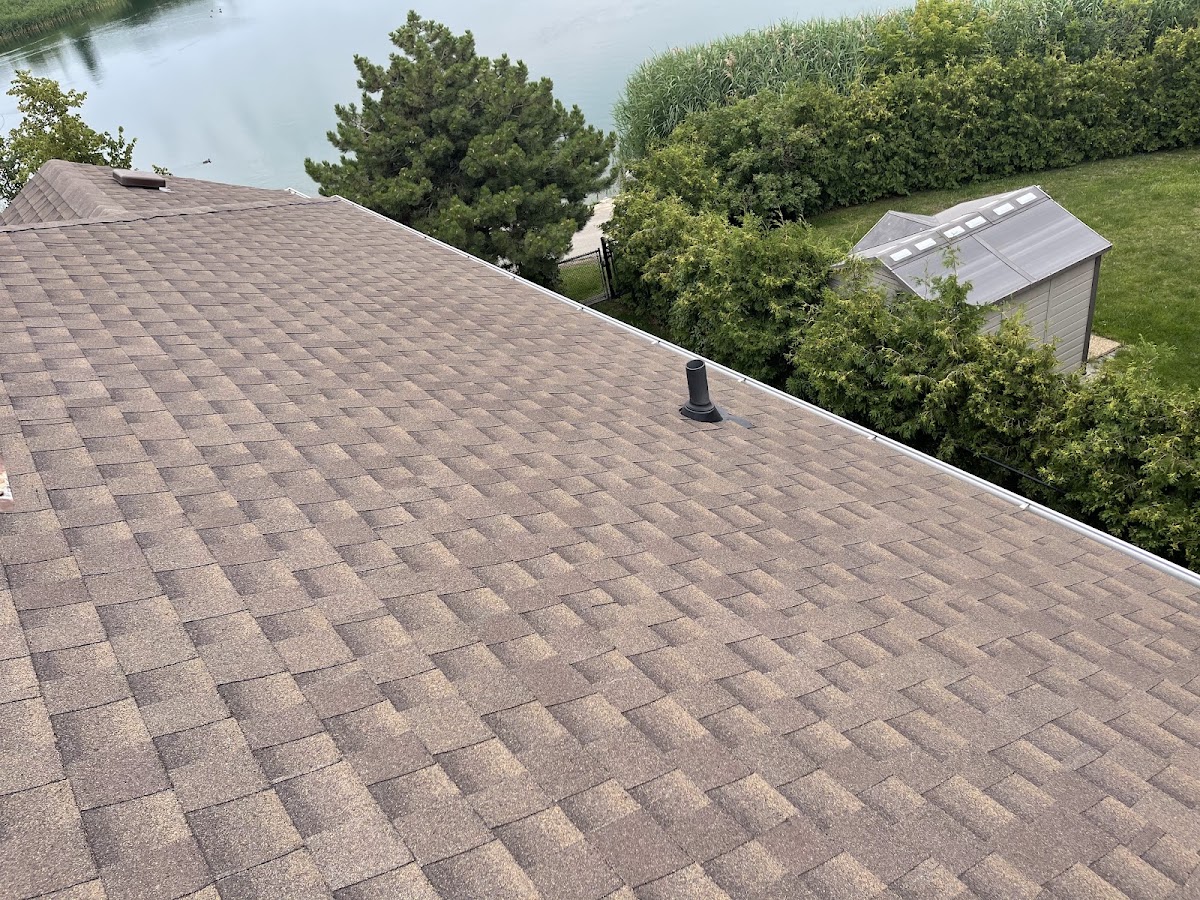 Newly finished brown shingle roof with a new vent stack overlooking a lake